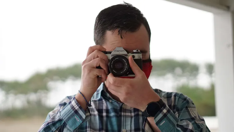 Photographer in plaid shirt and red mask holding vintage Canon film camera to eye