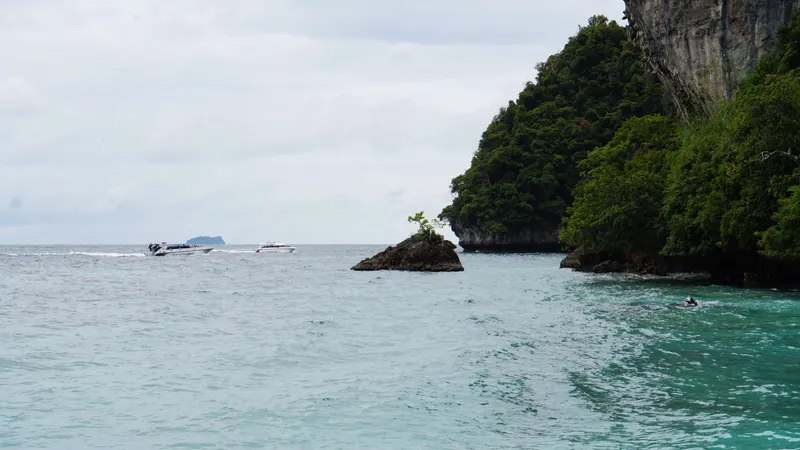 Tour boats in turquoise tropical ocean near limestone cliff and green island