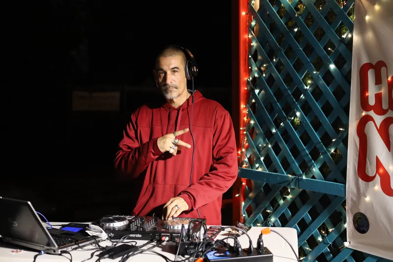 Male DJ in red hoodie performing live with headphones and mixing equipment at night