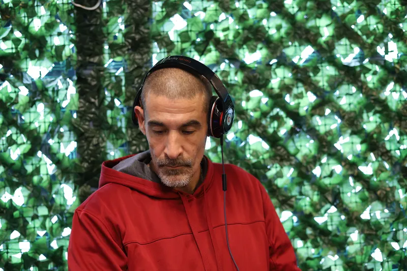 Man with beard wearing Beats headphones and red hoodie against green ivy wall
