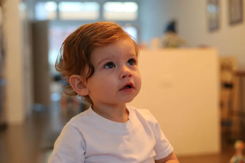 Curious toddler boy with curly red hair and big eyes looking upward
